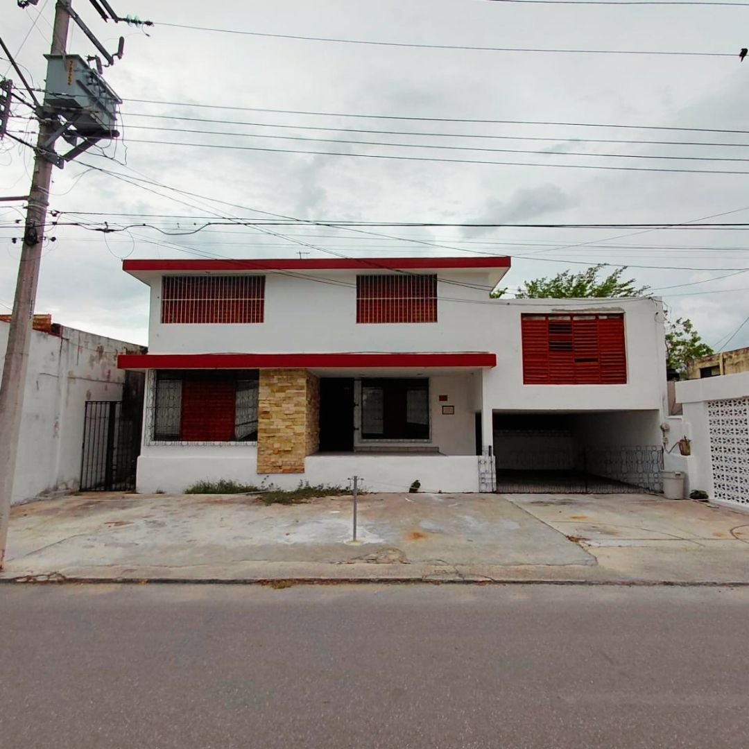 Two story white house with red trim and a stone column at the front a small porch a paved driveway and a covered garage on a residential street