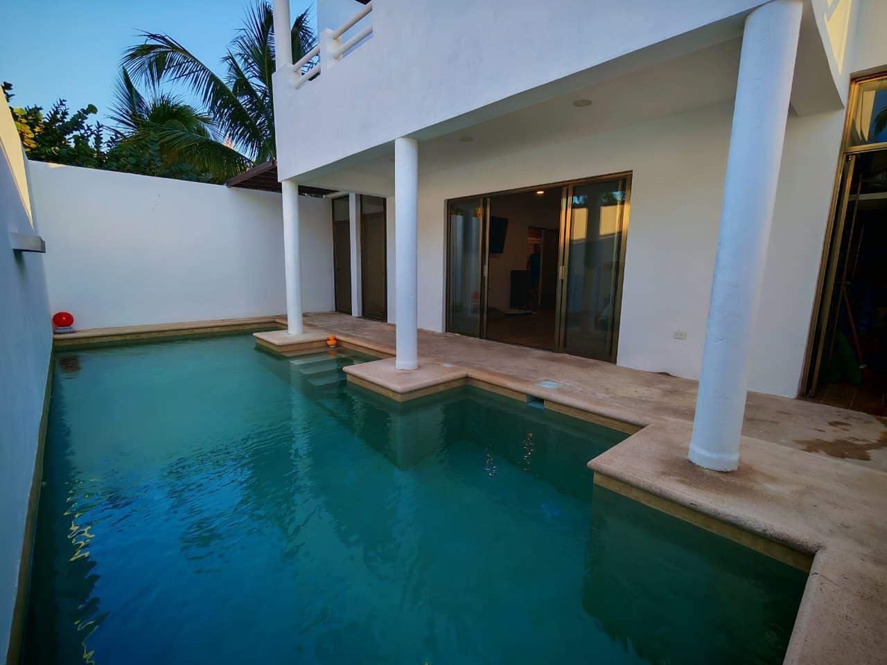 Backyard pool beside a white two story house with columns and sliding glass doors palm trees in the background