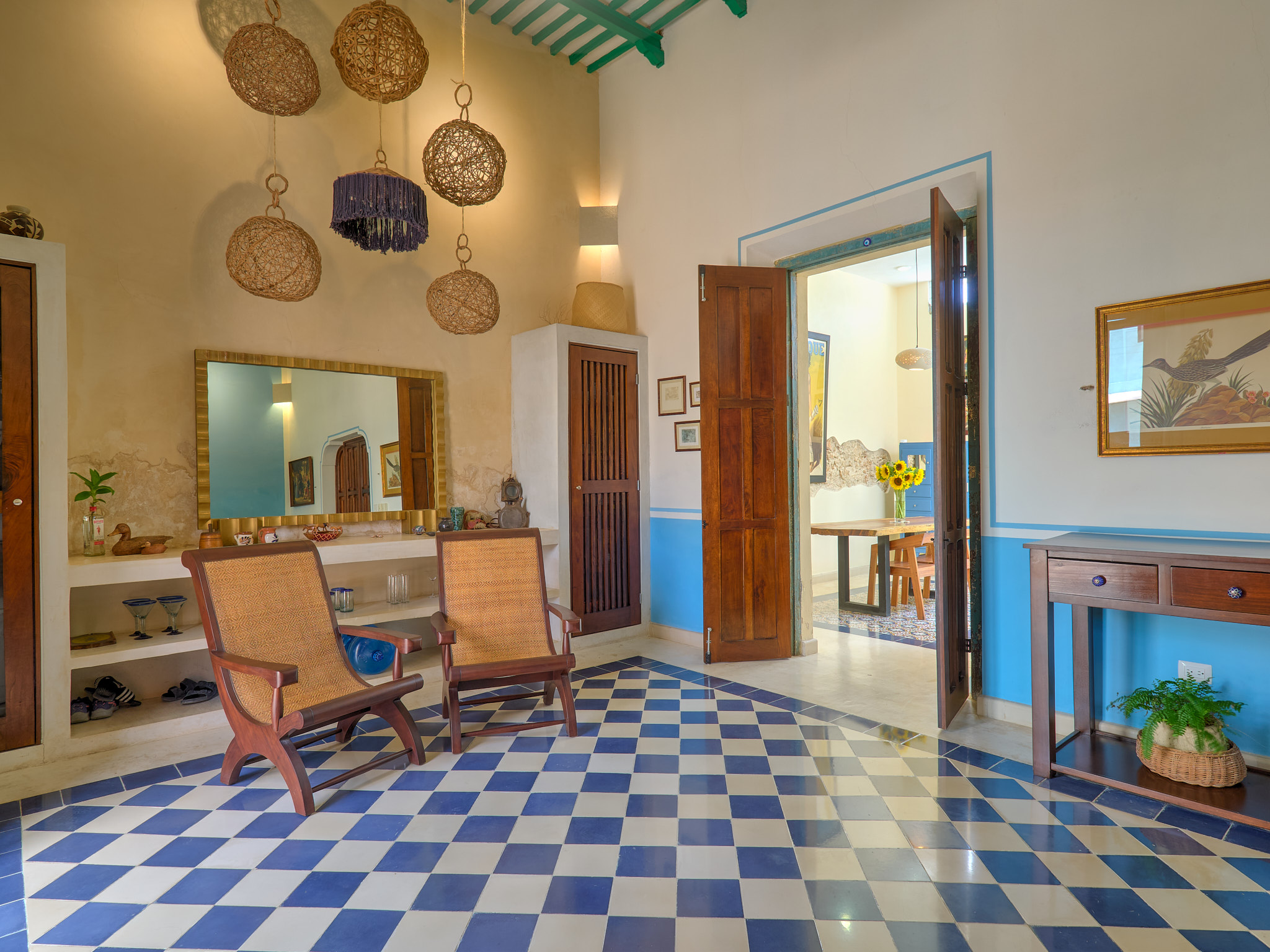 Living area with blue and white checkered floor woven pendant lamps and wooden chairs facing a wall mirror