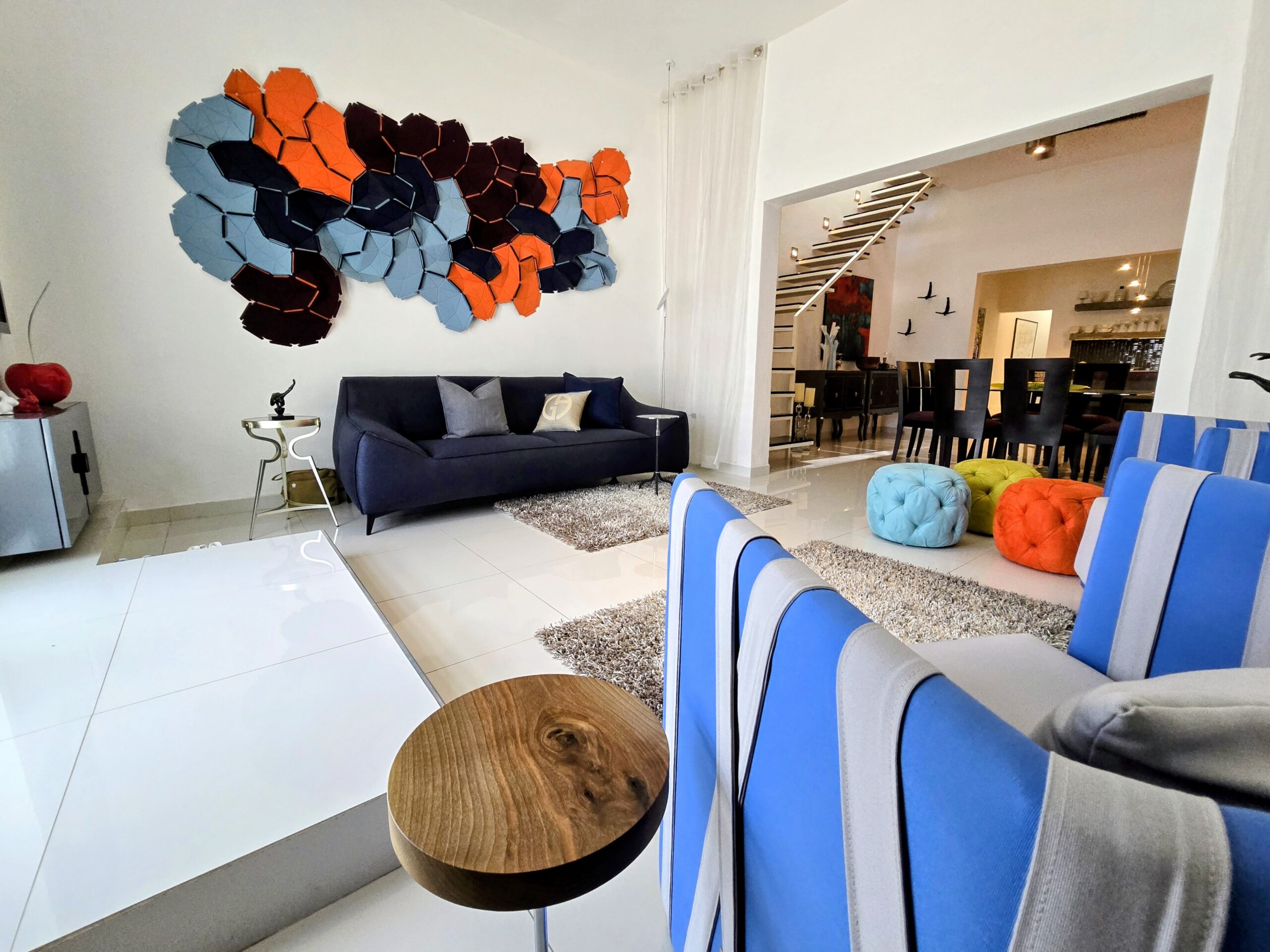 Living room with a dark sofa beneath a colorful geometric wall sculpture in orange blue and navy hues above