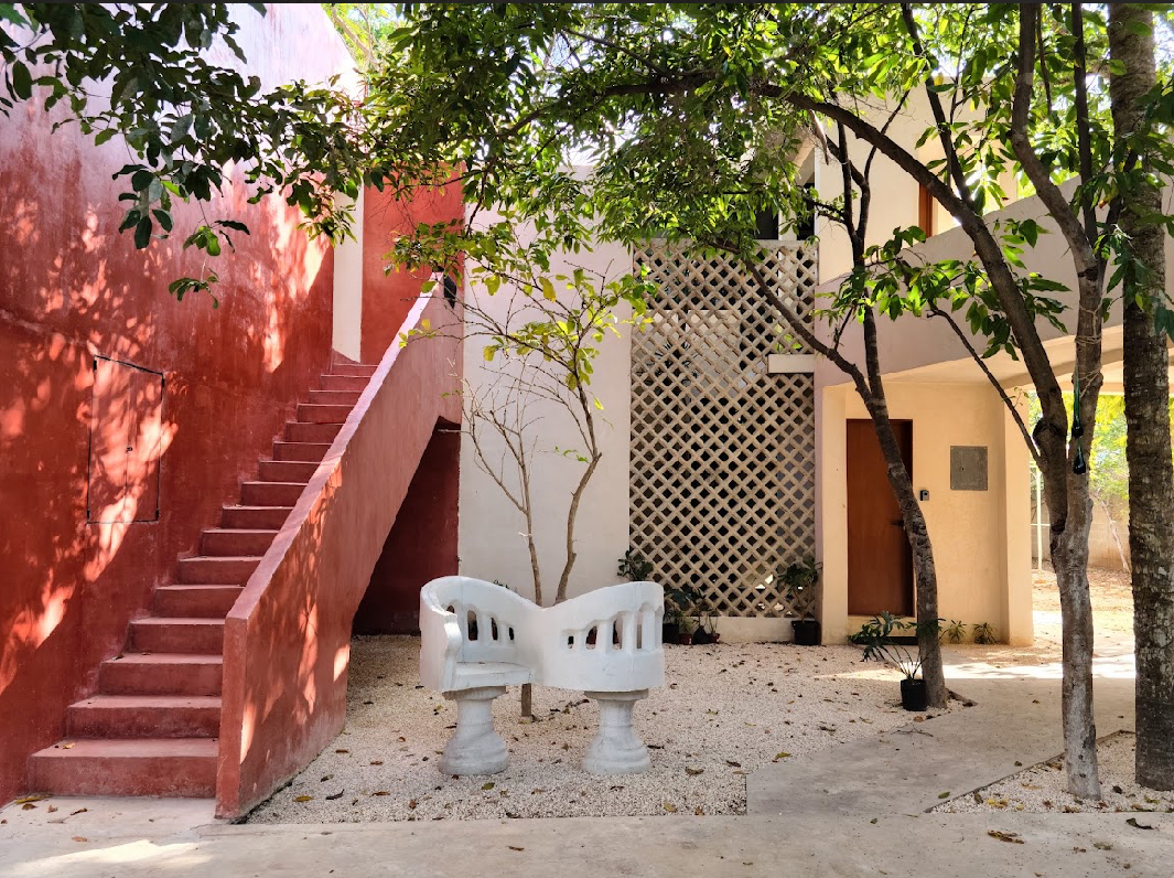Outdoor courtyard with a red stairway on the left beige walls and a white curved bench around a small tree