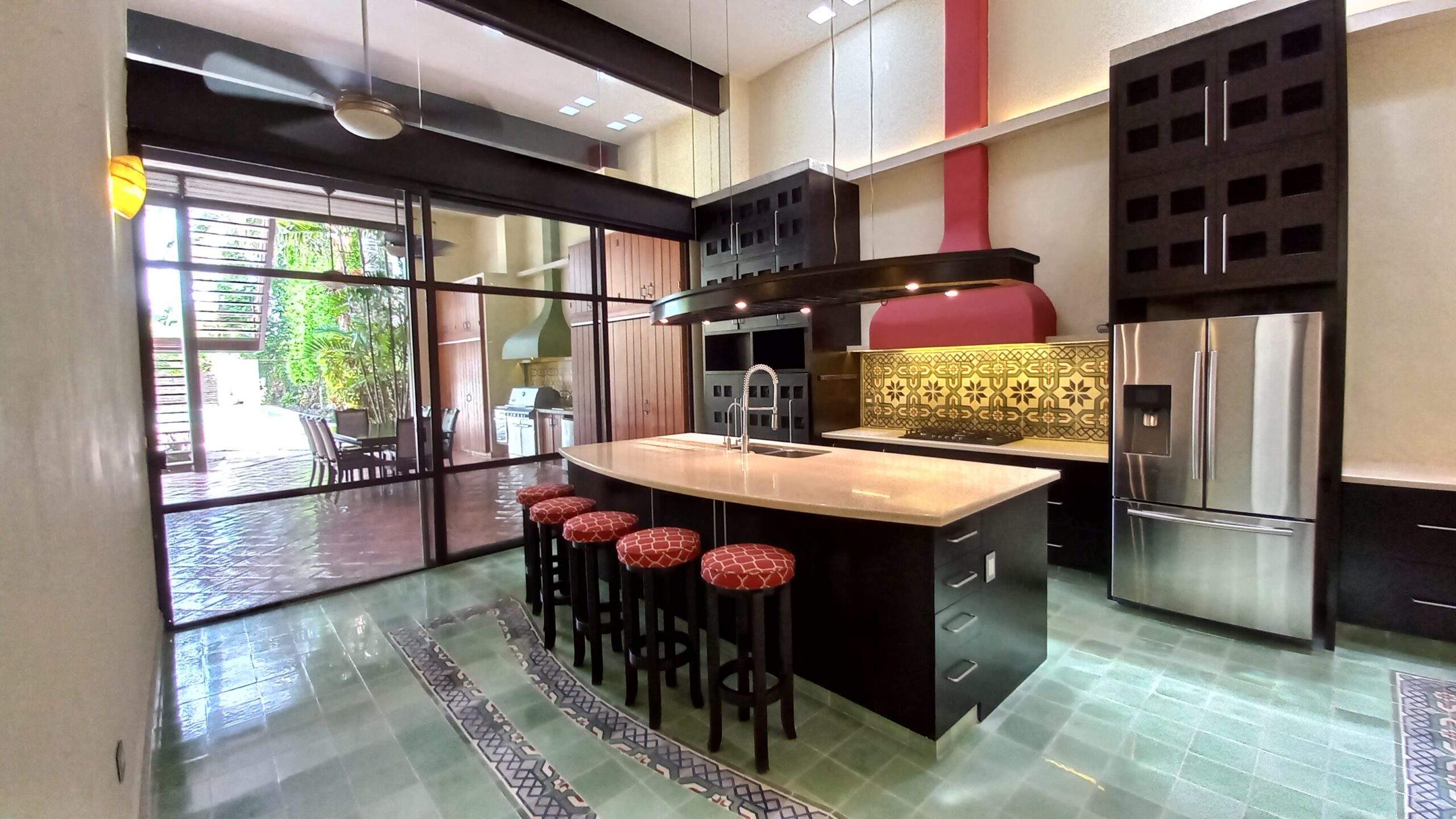Modern kitchen with a curved island red exhaust chimney black cabinets and stainless steel refrigerator glass doors open to an outdoor dining area