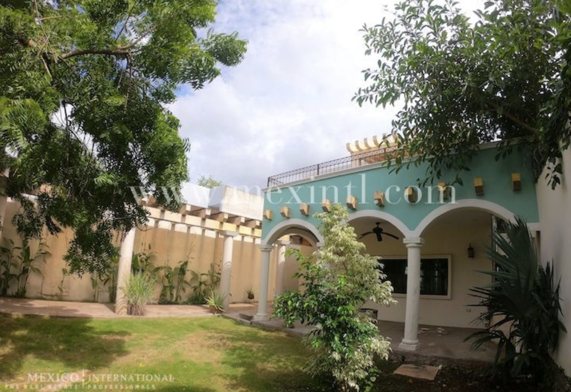 Courtyard of a home with turquoise archway white columns and lush green trees surrounding a small garden