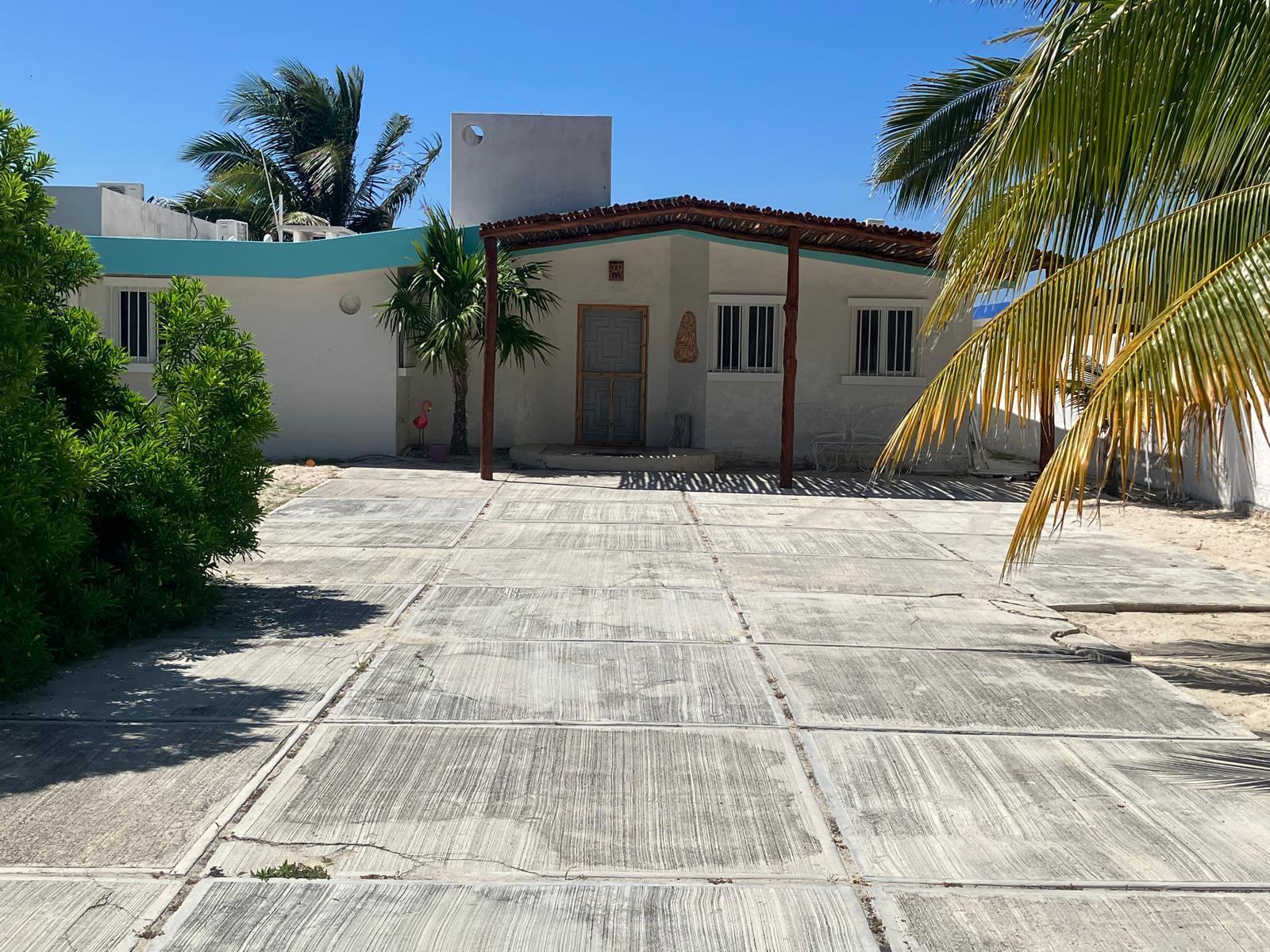 White one story house with turquoise awning concrete driveway and tropical plants under a clear blue sky